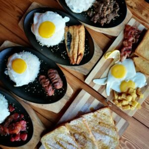 An appetizing breakfast spread featuring eggs, meats, toast, and rice on a wooden table.